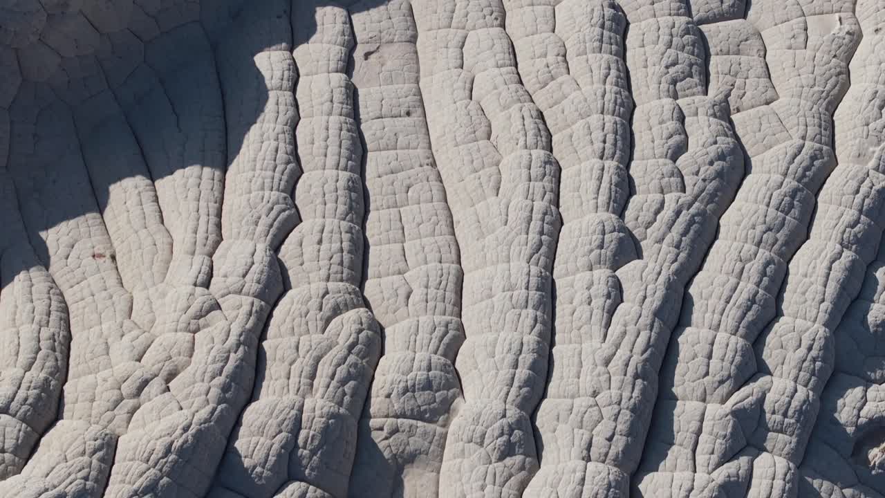 A top-down drone shot revealing the unique sandstone rock features of White Pocket Arizona surrounded by sandy desert and blue skies at sunset