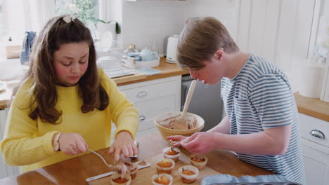 Pareja-Joven-Con-Síndrome-De-Down-Decorando-Pastelitos-Caseros-Con-Glaseado-En-La-Cocina-De-Casa