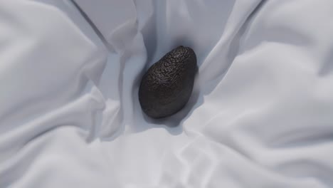 hipnotizante cámara lenta de un aguacate que desciende sobre una hoja blanca prístina, seguido de ser cuidadosamente envuelto, invocando una estética serena y minimalista