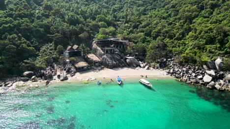 boats on an inlet with cabins in mango bay ko tao island thailand with tourists at beach, aerial descent tilt up shot