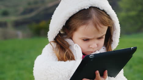 Ein-Süßes-Kleines-Mädchen-In-Einer-Lustigen-Weißen-Kapuze-Studiert-Das-Tablet