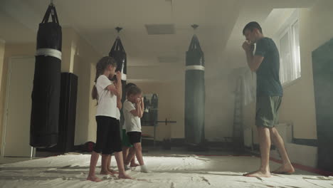 children stand in boxing stance with trainer in gym. little students learn self defence technique under sensei control in sports club slow motion