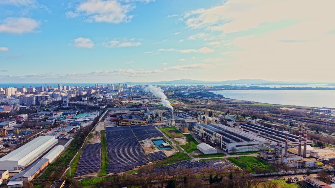 日中の水辺にある工業地帯、工場群と都市のスカイラインが見渡せる。