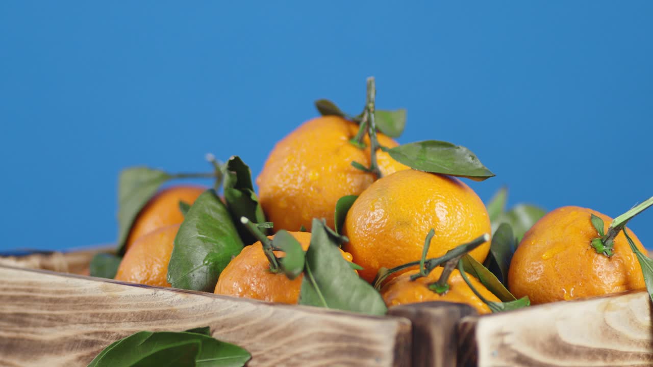 Fresh tangerines with leaves in wooden box slowly rotate.