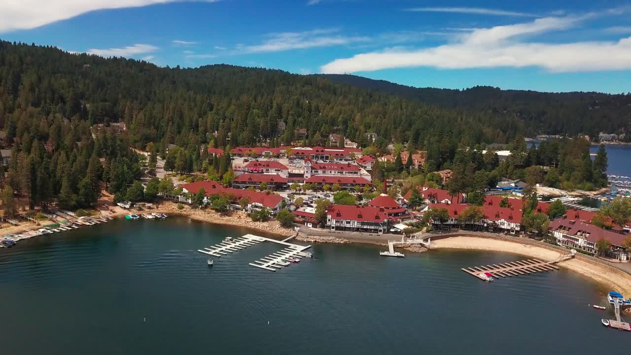 Aerial reverse pull back shot tilting up to reveal charming mountain village on lake. 4K