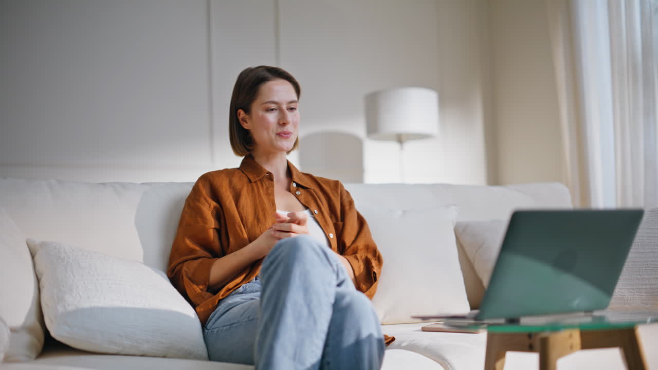 Online couch talking laptop web camera sitting apartment sofa. Smiling woman