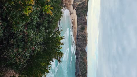 Zambujeira-do-Mar-over-the-sea-shore-with-ocean-waves,-cliffs-and-sand-dunes-covered-by-green-vegetation-red-leaves-of-sour-fig,-sunny-day,-clear-blue-sky