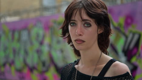 close up outdoor fashion portrait of young alternative style woman with eyebrow piercing in front of graffiti covered wall in london city street uk in real time 1