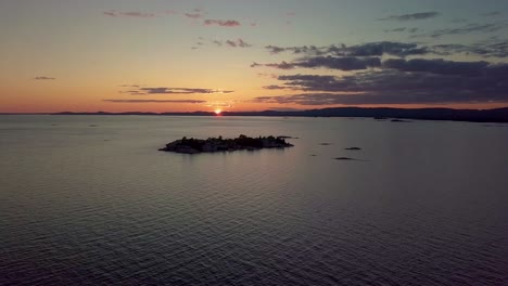 high view of rocky pine tree island in blue lake at sunset, drone aerial wide dolly out