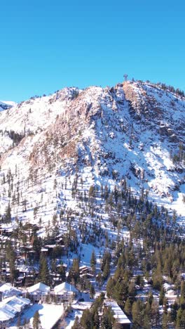 Vertical-Aerial-View,-Snow-Capped-Hills-Above-Olympic-Village-and-Palisades-Ski-Resort,-Lake-Tahoe-CA-USA