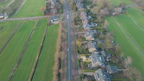 Volando-Sobre-Una-Carretera-Tranquila-Con-Poco-Tráfico-Junto-A-Una-Hilera-De-Casas-Independientes-En-Una-Zona-Rural