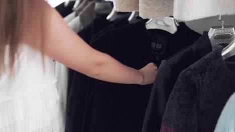 close-up handheld shot of a sexy shopper lady examining fur coats in a store