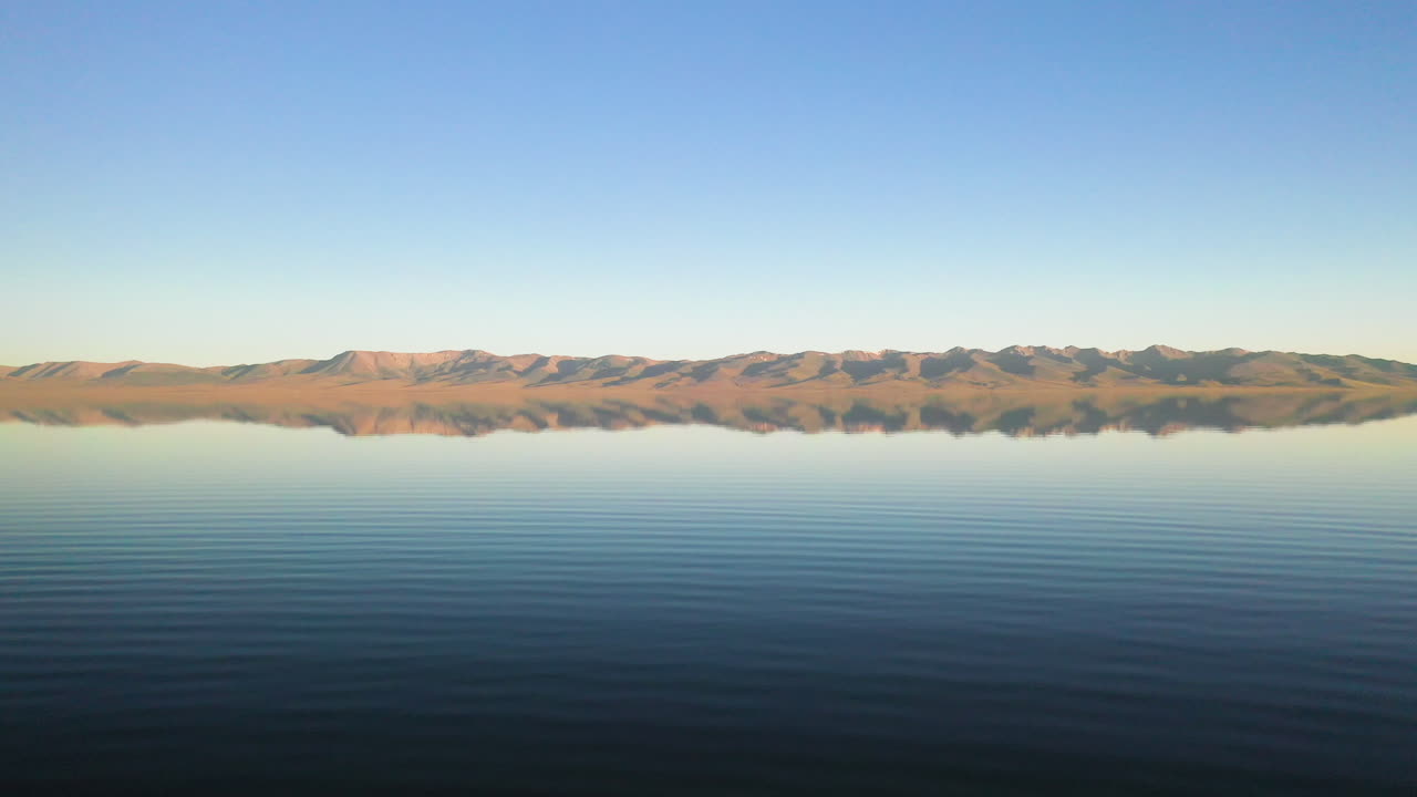 멀리 산이 있는 키르기스스탄의 송쿨 호수에서 수영하는 모험심 넘치는 남자에 대한 공중 촬영