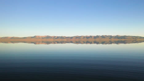 aerial shot over an adventurous man swimming in song kul lake in kyrgyzstan, with the mountains in the distance