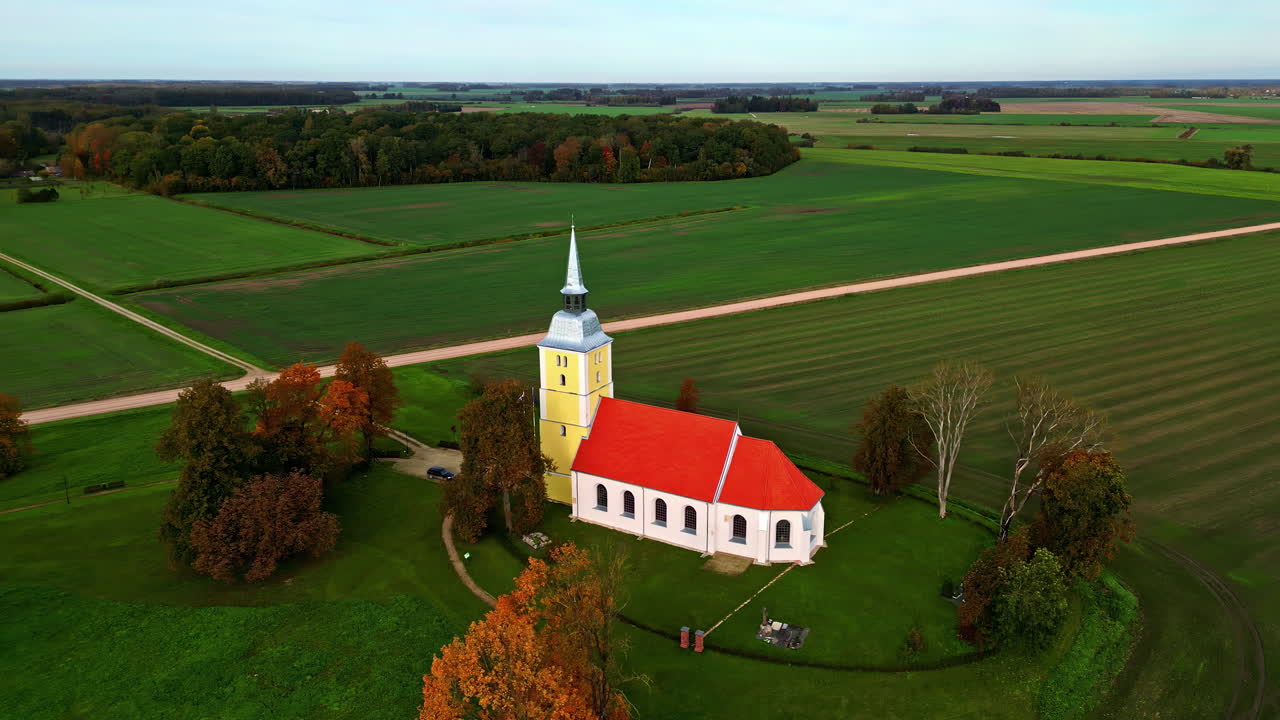 Mežotnes baznīca with red-orange roof and yellow tower, traditional Latvian countryside church