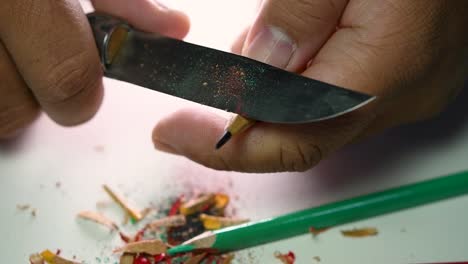 imágenes de manos afilando lentamente un lápiz y algunos lápices de colores con un cuchillo afilado