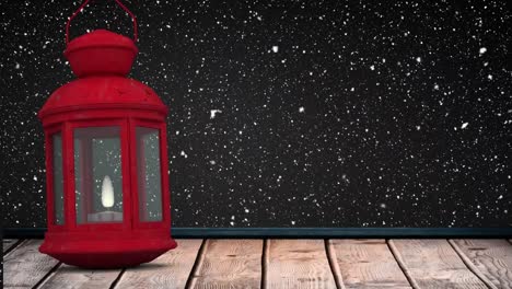 Digital-animation-of-snow-falling-over-red-christmas-lantern-on-wooden-surface-against-black-backgro