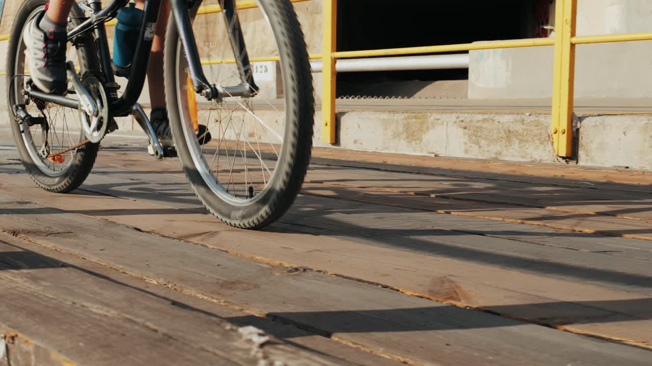 A person riding a bicycle on a sunny wooden deck with a yellow railing