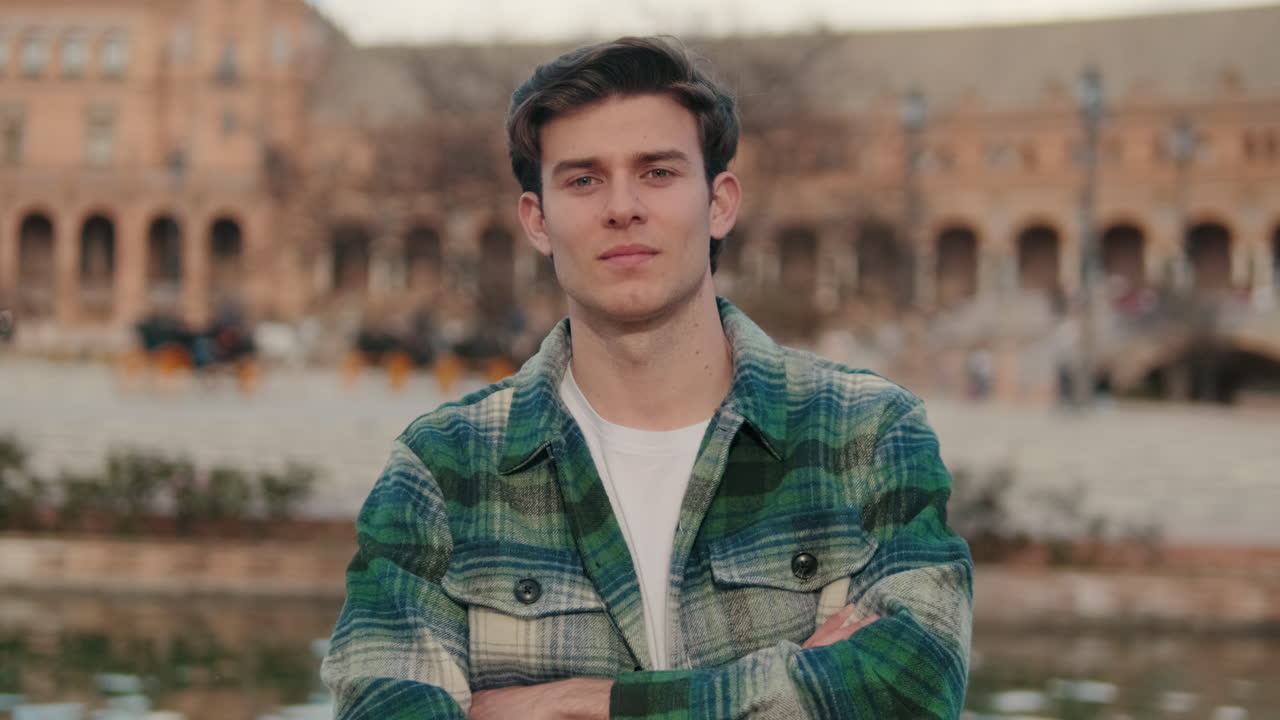 Young man crosses his arms looking at camera on old city background