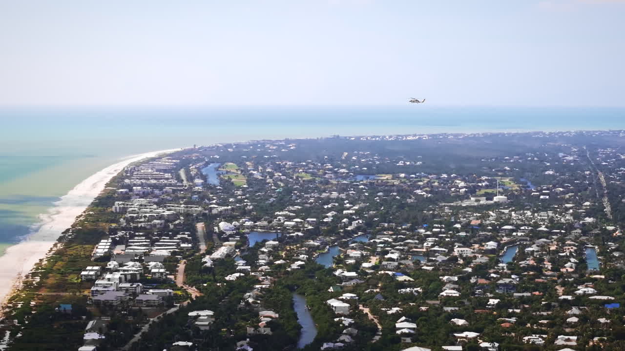 Florida'daki Sanibel Adası ve San Carlos Körfezi üzerinde bir helikopteri takip eden, kıyı suları boyunca yakınlaştırılmış bir pan ile sinematik yüksek irtifa 70mm havadan çekim.
