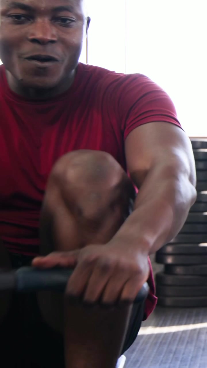 Vertical video: Gripping handle, man using rower, pulling handle in gym for cardio wearing red tee