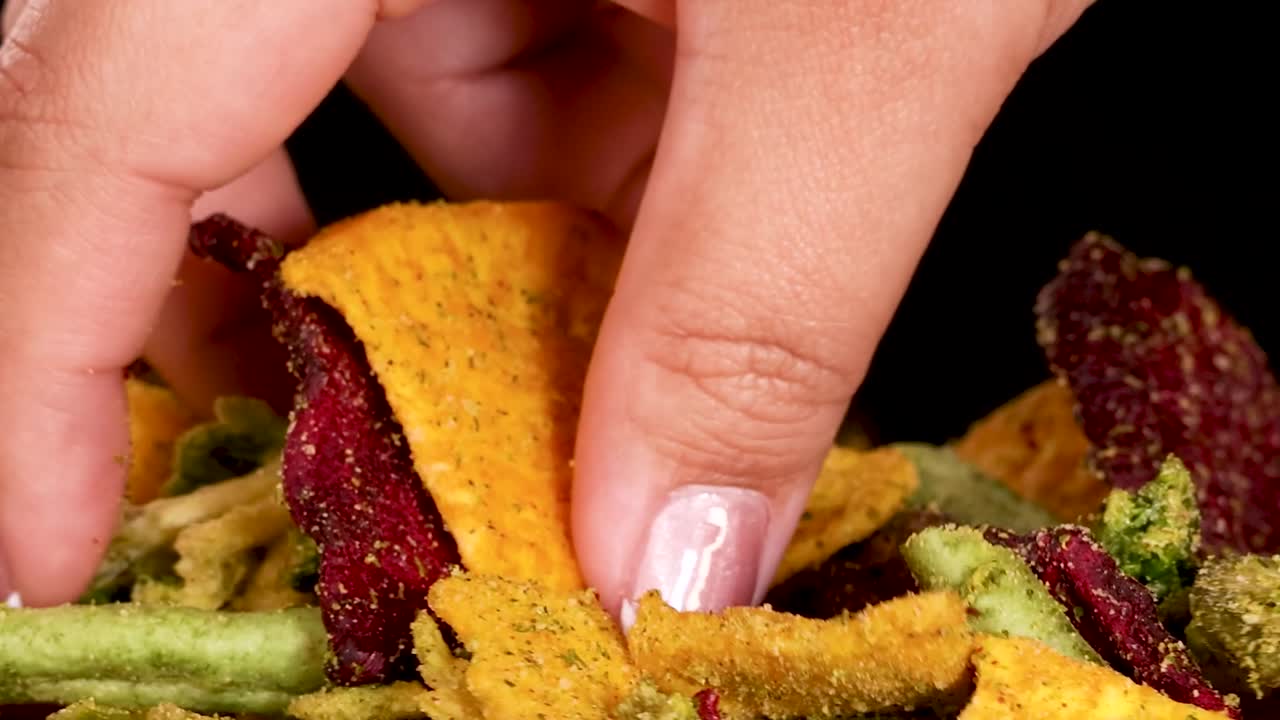 Un primo piano di dita che selezionano colorate chips di verdure essiccate da un mucchio.