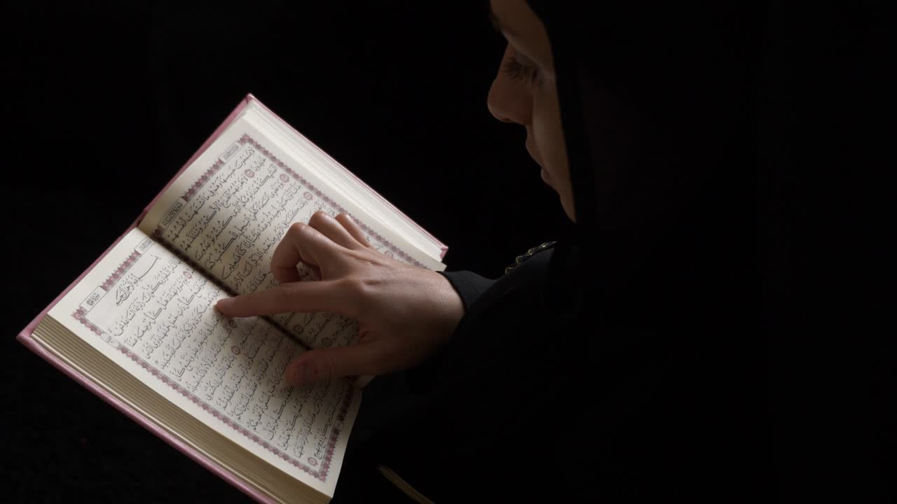 A Muslim woman in hijab holding her Quran and reads some verses from it