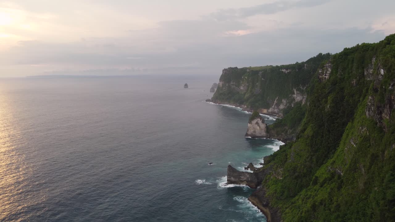Aerial Sunset view Tropical coastline of Nusa Penida Island high steep green cape cliffs and Coves overlooking the waves of indian ocean crashing downdiamond shaped rocks, Indonesia