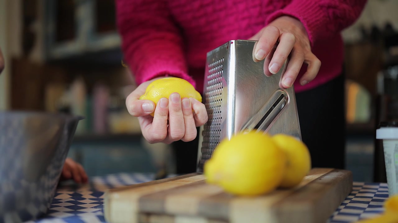 Mujer rallando cáscara de limón con un rallador en la mesa de la cocina para obtener ralladura de cítricos.