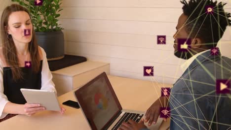 Animation-of-two-globes-of-digital-icons-spinning-over-diverse-man-and-woman-discussing-at-office