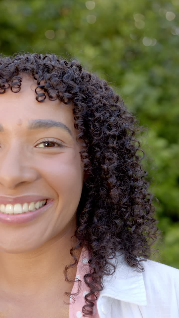 Vertical video: Smiling woman with curly hair enjoying outdoor time in garden