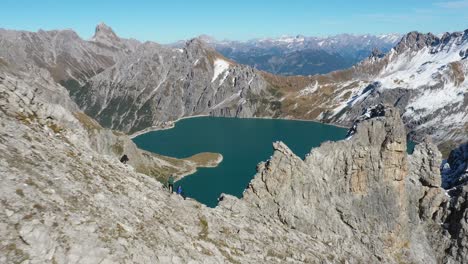 Toma-Aérea-De-Un-Grupo-De-Amigos-Sentados-Juntos-En-La-Cima-De-La-Montaña-Lunersee,-Mirando-El-Lago-Del-Corazón-Del-Amor-Después-De-Una-Larga-Caminata-Por-Los-Alpes-Suizos-Durante-Un-Viaje-De-Senderismo-De-Verano