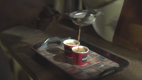 pouring hot milk tea or indian chai in plastic cups inside kitchen of an indian dhaba or restaurant