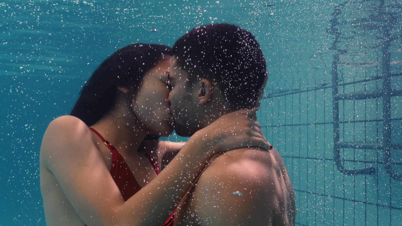 young couple kissing underwater in swimming pool enjoying intimate kiss  romantic lovers submerged in water floating with bubbles in passionate  intimacy