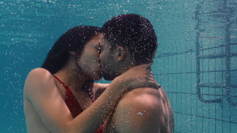 Pareja-Joven-Besándose-Bajo-El-Agua-En-La-Piscina-Disfrutando-De-Un-Beso-íntimo-Amantes-Románticos-Sumergidos-En-Agua-Flotando-Con-Burbujas-En-Una-Intimidad-Apasionada