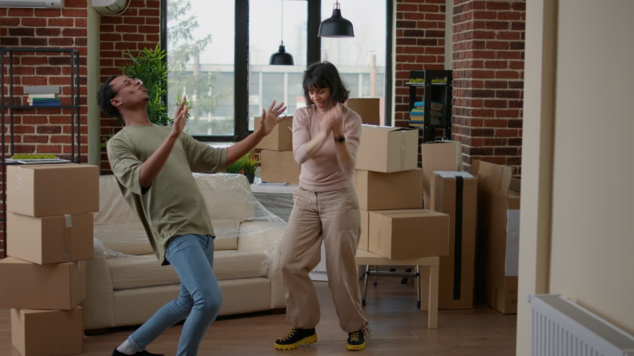 Cheerful couple dancing in new apartment celebrating relocation