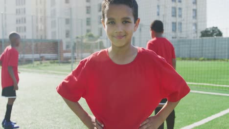 Mixed-Race-Fußballkind-In-Rot,-Lächelnd-Und-In-Die-Kamera-Schauend