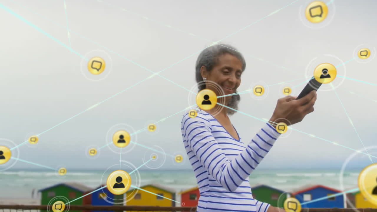 Animation of network of connections with icons over biracial woman using smartphone by sea