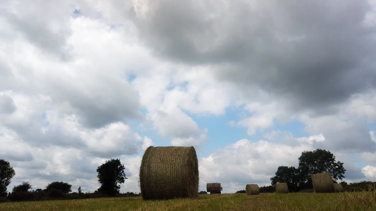 Timelapse of filed of hay bales being loaded on to a trailer using tractor