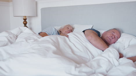 sleeping senior couple lying in bed at home together