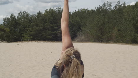 woman doing side yoga exercise in sand and lifting arm into the air