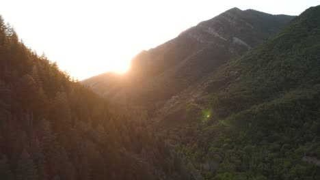 sunset sun rays peaking over mountain ridge in millcreek canyon, utah - aerial