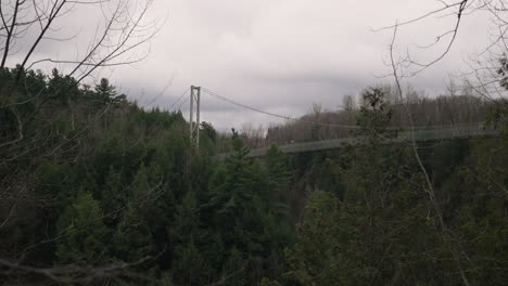 suspended footbridge above coaticook river valley with lush foliage in quebec, canada, rack focus shot