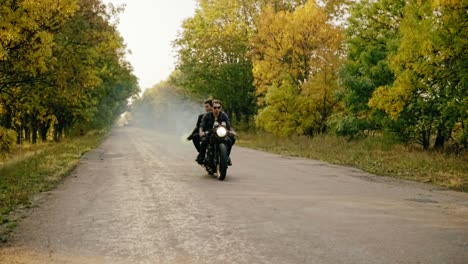 Schöner-Mann-Mit-Sonnenbrille,-Der-Im-Herbst-Mit-Seiner-Freundin-Auf-Einem-Motorrad-Auf-Der-Asphaltstraße-Im-Wald-Fährt.-Seine-Freundin-Ist