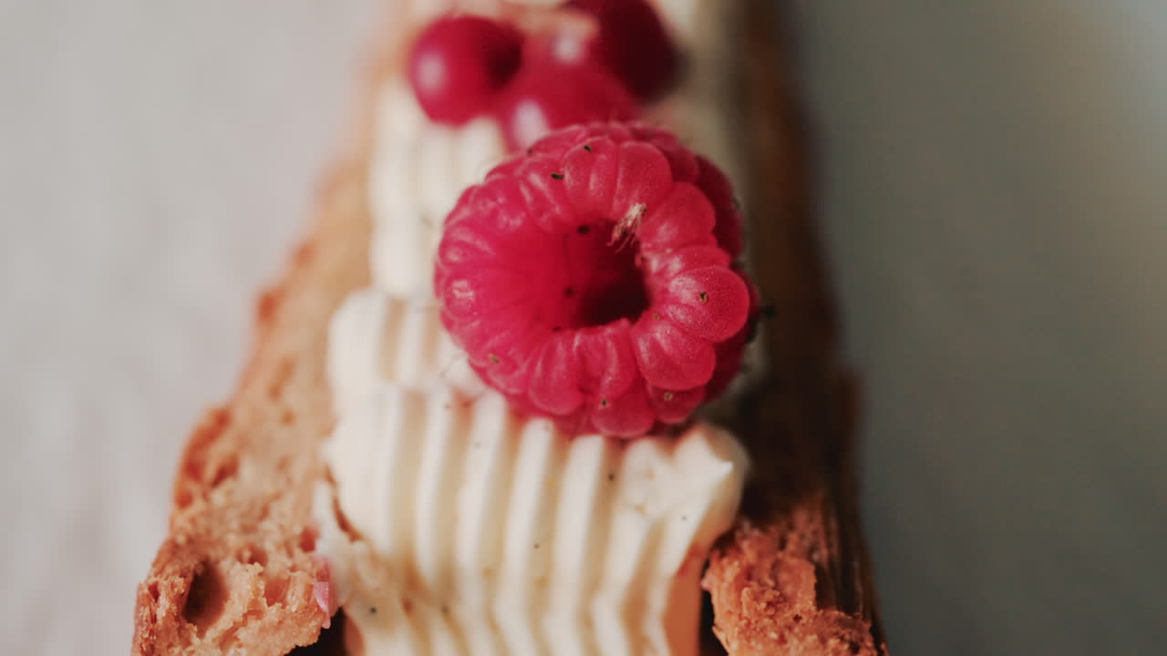 Close up of a gourmet pastry topped with cream, raspberries, and red currants