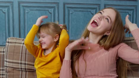 Mother-and-little-child-kid-daughter-having-fun-sitting-on-sofa-ooling-around,-making-faces-at-home