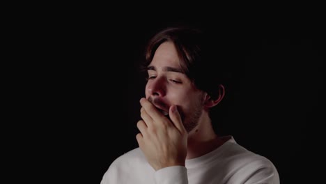 trendy young man yawning, tired gesture, close, black background