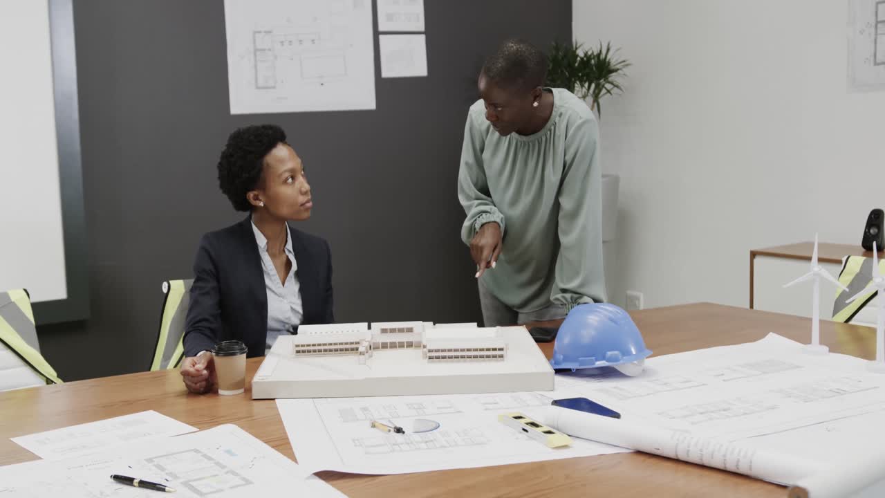 African american female architects discussing blueprints in office, in slow motion