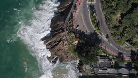 antena de arriba hacia abajo que muestra el estacionamiento del mirador de leblon en la avenida niemeyer con un amplio sendero para bicicletas a un lado de las olas rompiendo en la playa de rocas