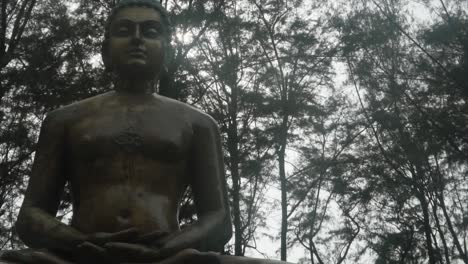 estatua de una persona con la luz del sol brillando a través de las copas de los árboles